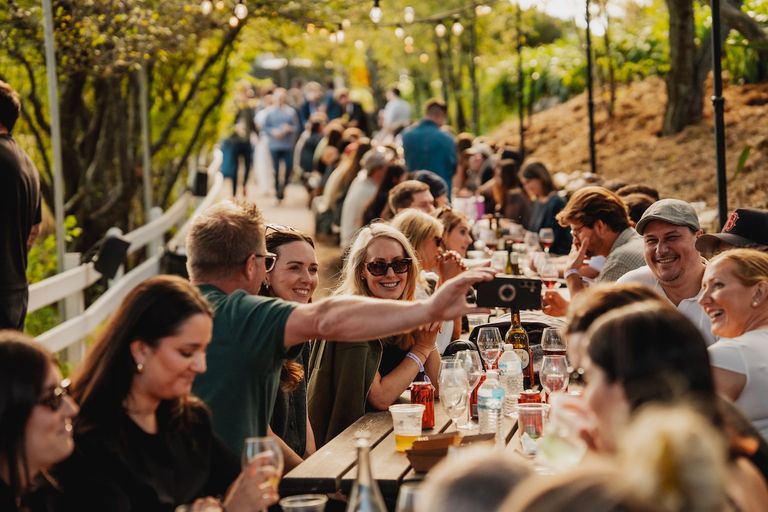 Guests enjoying drinks and taking photos at long outdoor dining tables during The Scenic Harvest Party at The Scenic Hotel.